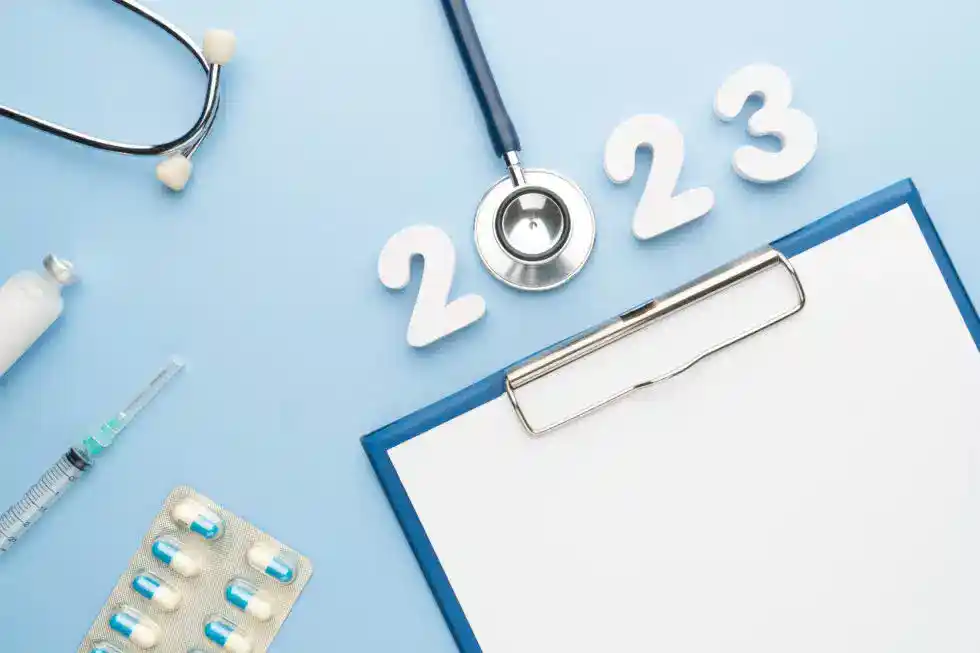 Stethoscope with doctor order chart, prescription, pills, syringe, vaccine vial and white number 2023 on table blue background.